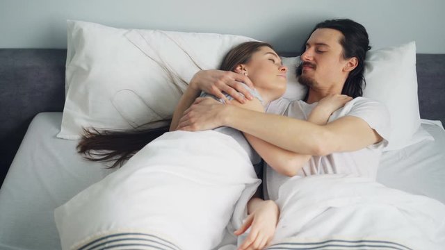 Man and woman young couple are lying in bed hugging talking enjoying bedtime together in apartment bedroom. Relationship, relaxation and happiness concept.