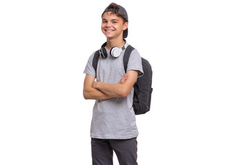 Happy teen boy in cap with headphones and backpack, isolated on white background. Smiling child...