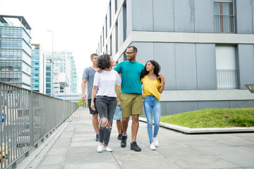 Happy joyful close friends enjoying outdoor walk. Mix raced people walking down urban street, hugging each other and talking. Friendship or unity concept