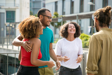 Mix raced group of people having fun and spending great time outdoors. Close interracial friends meeting on outdoor building terrace, hugging, chatting and laughing. Friendship and leisure concept