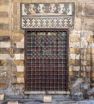 Wooden grunge window with decorated iron grid over stone bricks wall