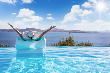 Sommerurlaub Konzeot: Frau auf einer Luftmatratze im Infinity Pool streckt vor Freude die Arme in...