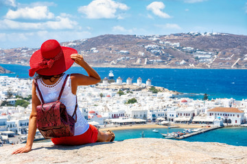Touristin mit Sonnenhut und Rucksack sitzt auf einem Hügel über der Stadt von Mykonos und...