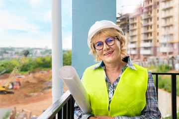 Builder woman at construction site in a green vest and a white helmet with the drawings....
