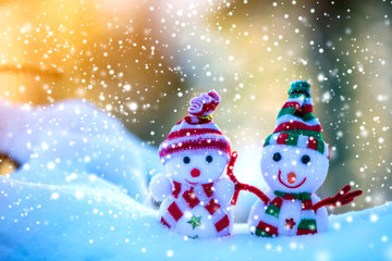 Two small funny toys baby snowman in knitted hats and scarves in deep snow outdoors on bright blue and white copy space background. Happy New Year and Merry Christmas greeting card.