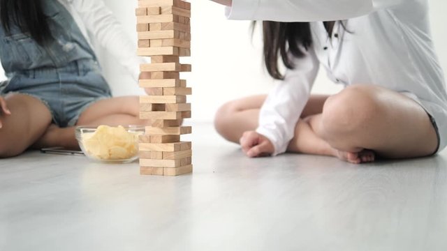 Happy Asian teenager girls playing wooden block stacks on the floor, lifestyle concept.