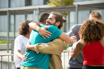 Happy guys in casual hugging each other. Close friends meeting on outdoor building terrace,...
