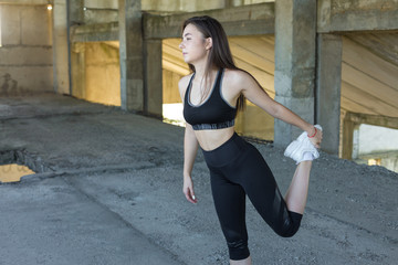 Slim athletic girl performs stretching exercises on the roof of an unfinished building, urban background.