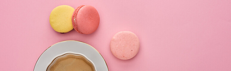 top view of delicious French macaroons near coffee in cup on saucer on pink background, panoramic shot
