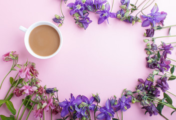 Pink and purple columbine flowers and a cup of coffee on pastel pink background.