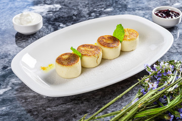 Cottage cheese pancakes served on white plate with hot sour cream marble table. Traditional homemade ukrainian food Syrniki. Gourmet Breakfast. Dessert cuisine