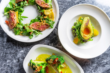 Top view green style salad on marble table. Three different salad with beef tataki, grilled avocado and brocolli on white plate. Tasty restaurant food style. Flat lay for recipe or banner