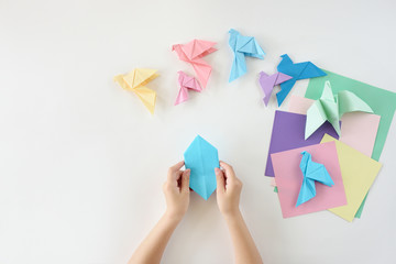 Children's hands do origami from colored paper on white background. lesson of origami
