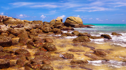 Boulders, the surf, and the blue sky over the sea, Karon sandy beach, Thailand