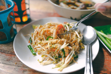 close up pad thai noodle thai street food on wooden table with hand and fork