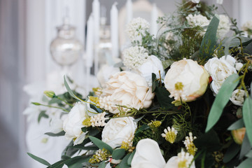 a bouquet of white roses, peonies, dahlias and eucalyptus branches and candles on the bedside table