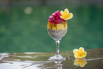 Chia seeds pudding with red dragon fruit and white yogurt in a glass for breakfast on the background of the swimming pool water. The concept of healthy eating.