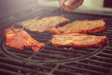 marinaded meat is grilled on a hot cast-iron grate - down-to-earth food and barbecue party concept - foreground and background with tongs and hand blanked out blurry