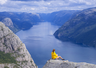 Girl in yellow jacket looking at Lysefjord fjord from Preikestolen, Norway