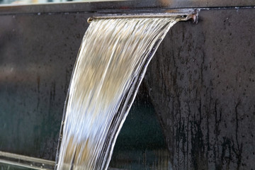 Natural water stream falling from a fountain in a city park. Concept, a falling jet of water.