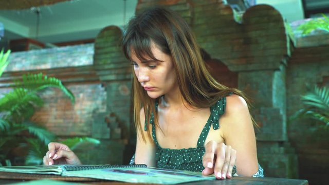 A girl in a summer terrace on the island of Bali chooses food on the menu.