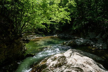 Naklejka na ściany i meble mountain river flowing on the rocky bottom of the river, having a white color, surrounded by trees, on a sunny day, with clouds in the sky. Spring view of the Crimean mountains.