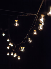 Incandescent lamps dimly shining hang in the form of a garland on wires, against the background of darkness.