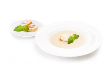 Plate with cream soup with a grenka and pieces of white loaf with cheese and the ground fat on a white saucer.