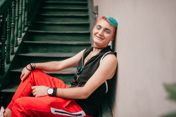 Happy gay man with colorful hairstyle in stylish clothes sitting on stairs