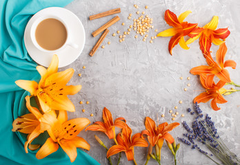 Orange day-lily and lavender flowers and a cup of coffee on a gray concrete background, with blue textile. top view.