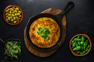 Spanish tortilla with vegetables and herbs on frying pan on blackboard background