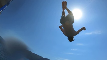 Handsome young man jumping from a boat or yacht into the sea or ocean. Summer vacation with friends. Tourists have fun and dive. Slow motion.