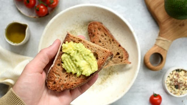 Spread avocado on toasted bread. Male hands making tasty avocado toast for breakfast, table top view