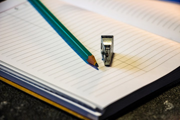 Sharpened pencil lies on a notebook, top view. Black background. Pencil planer. Close-up.