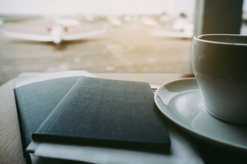 Airport business lounge. Two passports and electronic flight tickets lying on the table near the coffee cup with airplanes at terminal gate ready to takeoff.