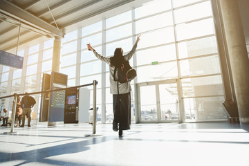 Fototapeta na wymiar Freedom of traveling. Happy girl tourist wearing casual clothes holding her hands up towards the sun at the airport terminal.