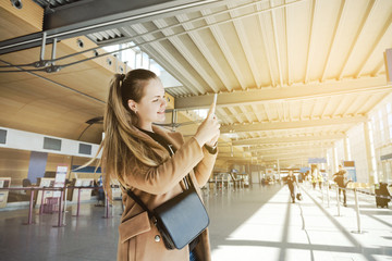 Happy young smiling cheerful female traveler taking photos on her phone at the airport while traveling to Europe.