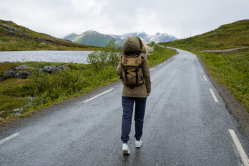 Girl with a backpack walking on an empty road enjoying scenic views. Lake and rocks landscape....