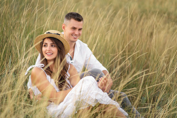 Young couple in love having fun and enjoying the beautiful nature. They sitting at the grass in the meadow