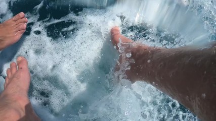 Handsome young man sits with his legs down from a boat or yacht in the sea or ocean. Plays with water, flying spray. Summer holidays with friends. Slow motion