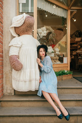 Fototapeta premium Beautiful young brunette female embracing big plush toy bear in white nightie on street
