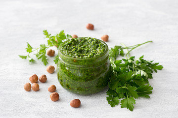 Fresh homemade parsley pesto with hazelnuts in glass jar on light gray background. delicious vegan food	