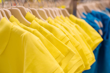 Shirts of yellow color on hangers in shop, selective focus