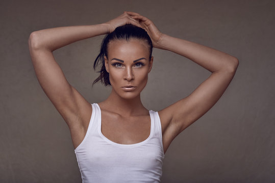 Sensual beautiful slim middle-aged woman in summer top posing with one hand to her chest and the other raised to her head as she looks at the camera with a serious expression