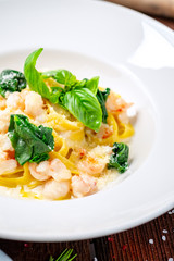 Tagliatelle with seafood. Traditional Italian pasta with shrimp, Basil in cream sauce on a white plate. Macro