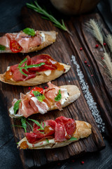 Traditional Bruschetta with Parma dried ham and prosciutto. Italian antipasti set sandwiches with jamon, cottage cheese, arugula, and sun-dried tomatoes on a rustic wooden Board, Close up