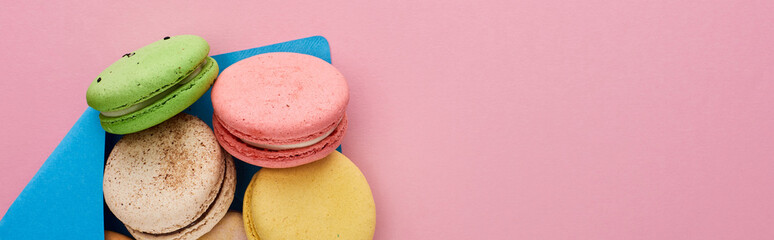 top view of multicolored delicious French macaroons in blue postal envelope on pink background with copy space, panoramic shot