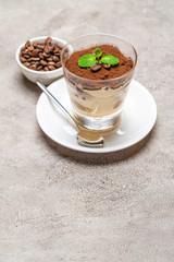 Classic tiramisu dessert in a glass cup on plate and coffee beans on concrete background