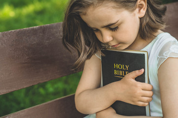 Reading the Holy Bible in outdoors. Christian girl holds bible in her hands sitting on a bench....