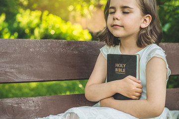 Reading the Holy Bible in outdoors. Christian girl holds bible in her hands sitting on a bench....